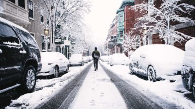 En väg som är täckt av snö. En människa går på vägen mellan några bilar.