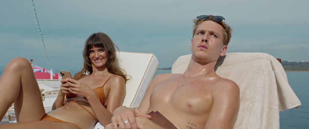 En bild ur en filmscen där två personer solar.